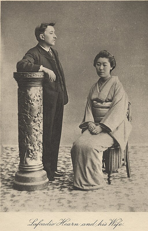 写真。左を向き立っている小泉八雲。右には椅子にすわったセツ。